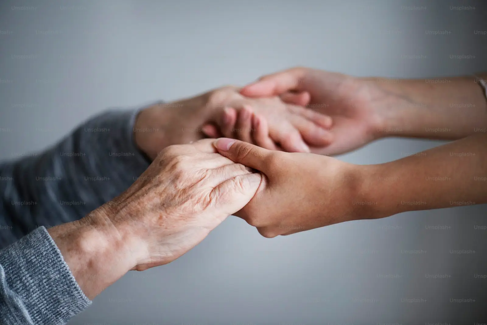 Jüngere Hände halten stützend die Hand eines älteren Menschen – Betreuung im eigenen Zuhause