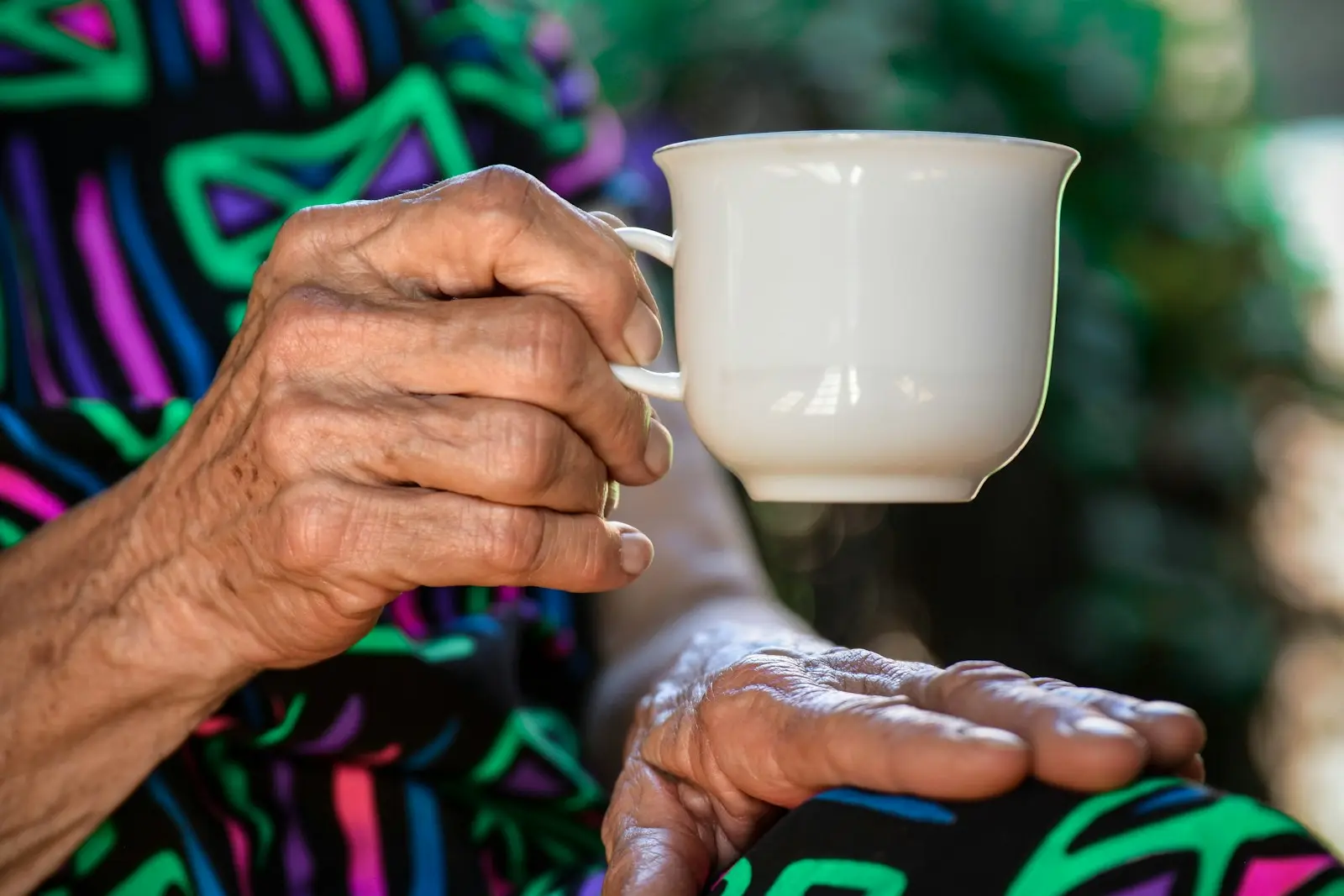Hände einer älteren Frau halten eine Tasse Tee im Tageslicht – gut versorgt auf Zeit