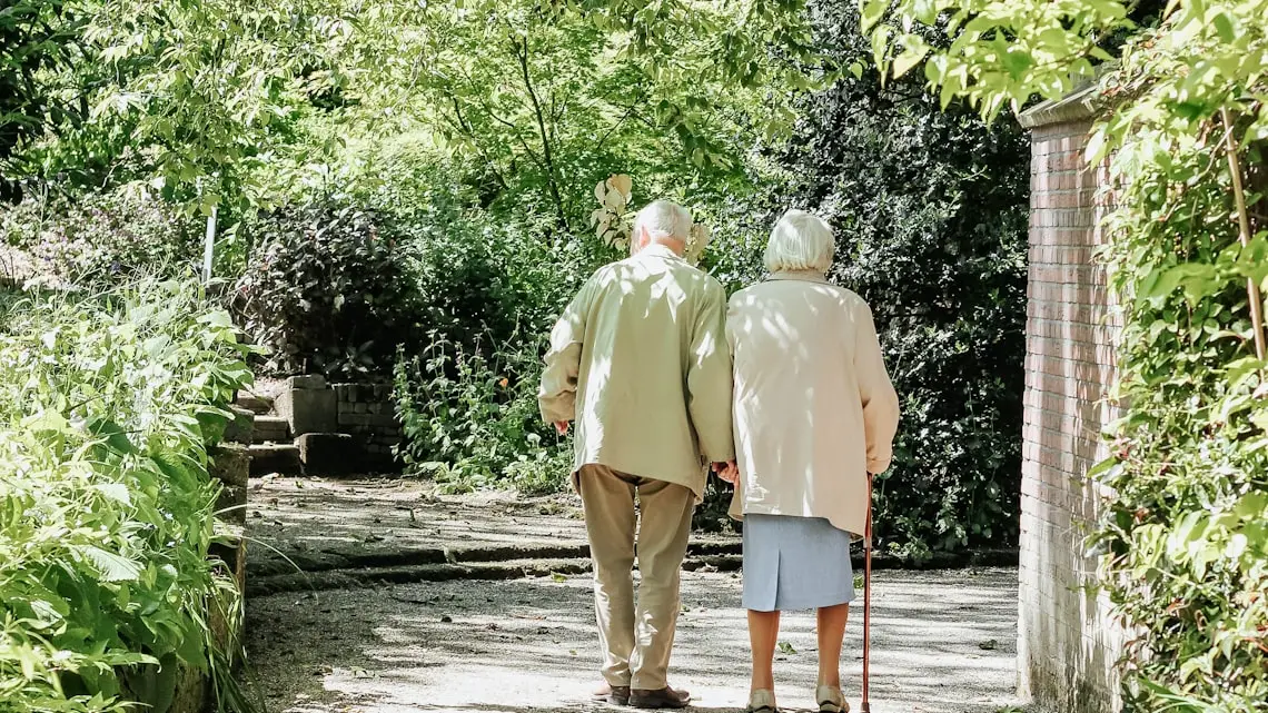 Älteres Paar spaziert an einem sonnigen Tag durch einen grünen Park – Zeit für eine Pause von der Pflege